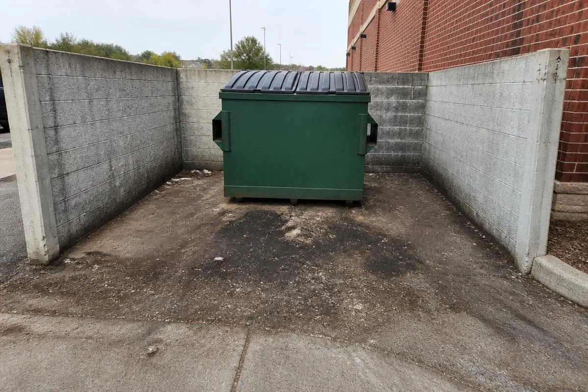 Commercial dumpster pad with heavy grime, stains, and debris residue before cleaning